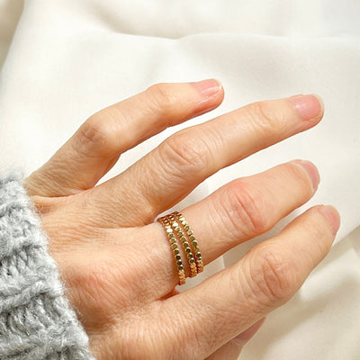 three layered 14K gold filled dot stacking rings on woman's finger. 14K Gold filled dot ring on solid white background. The dot ring is a series of uniform gold circles joined together to create a circle finger ring. Highly polished giving a glorious shine