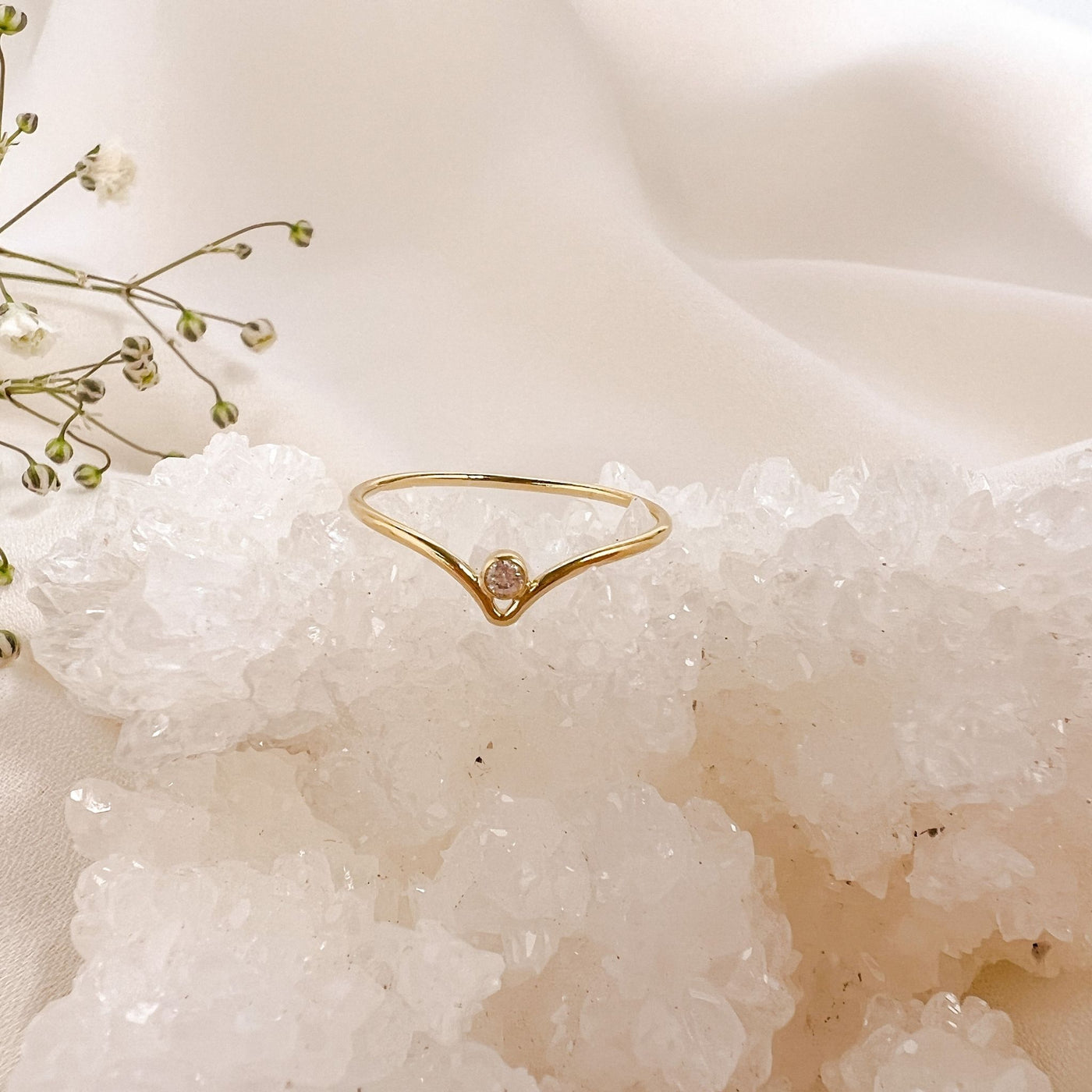   14K gold filled chevron shaped ring with white sparkly cubic Zirconia stone nestled into the centre point of the chevron peak. Ring is displayed onto of a white sparkly crystal geode with a pink background 