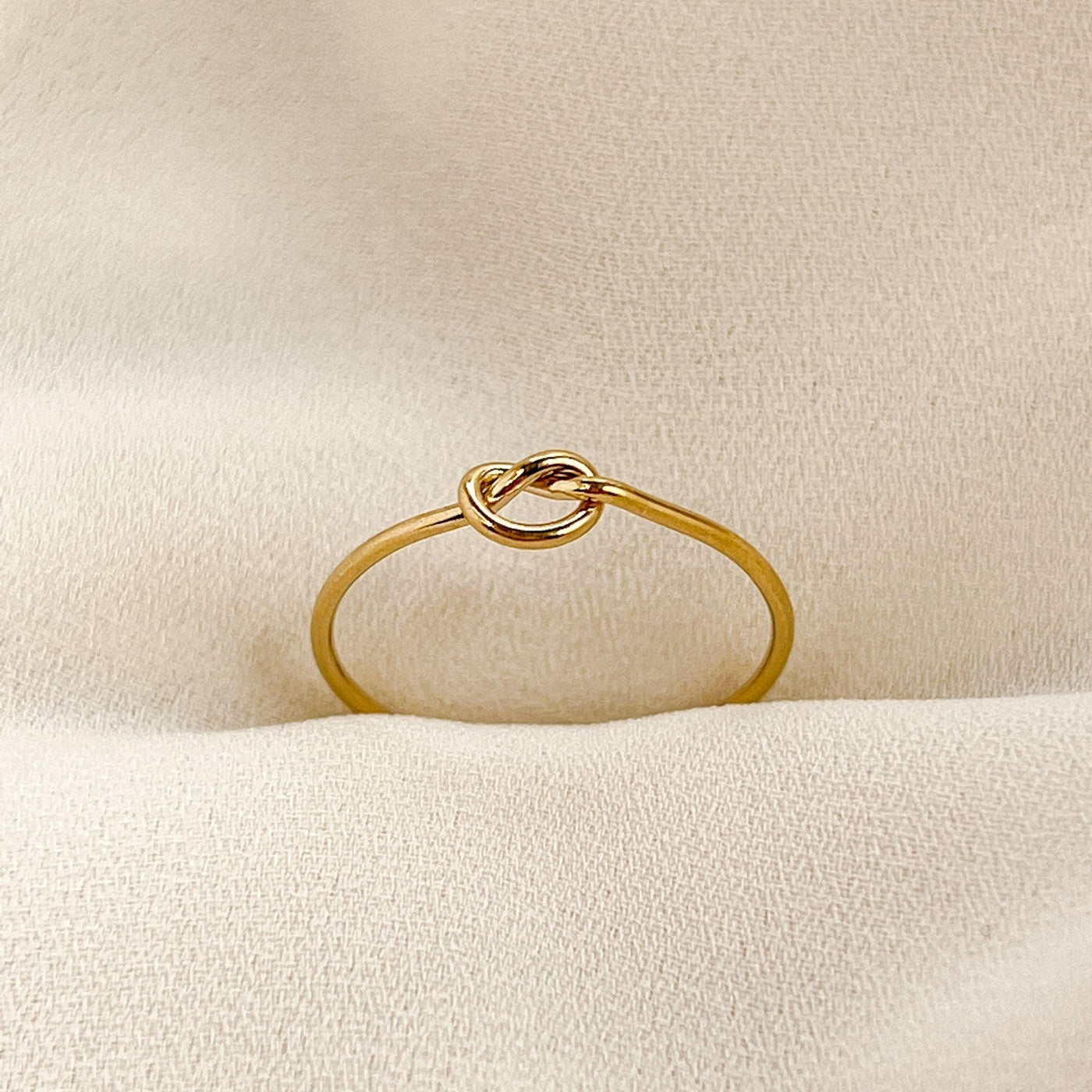14K gold filled band ring with knot shaped accent. Ring is on cream coloured fabric