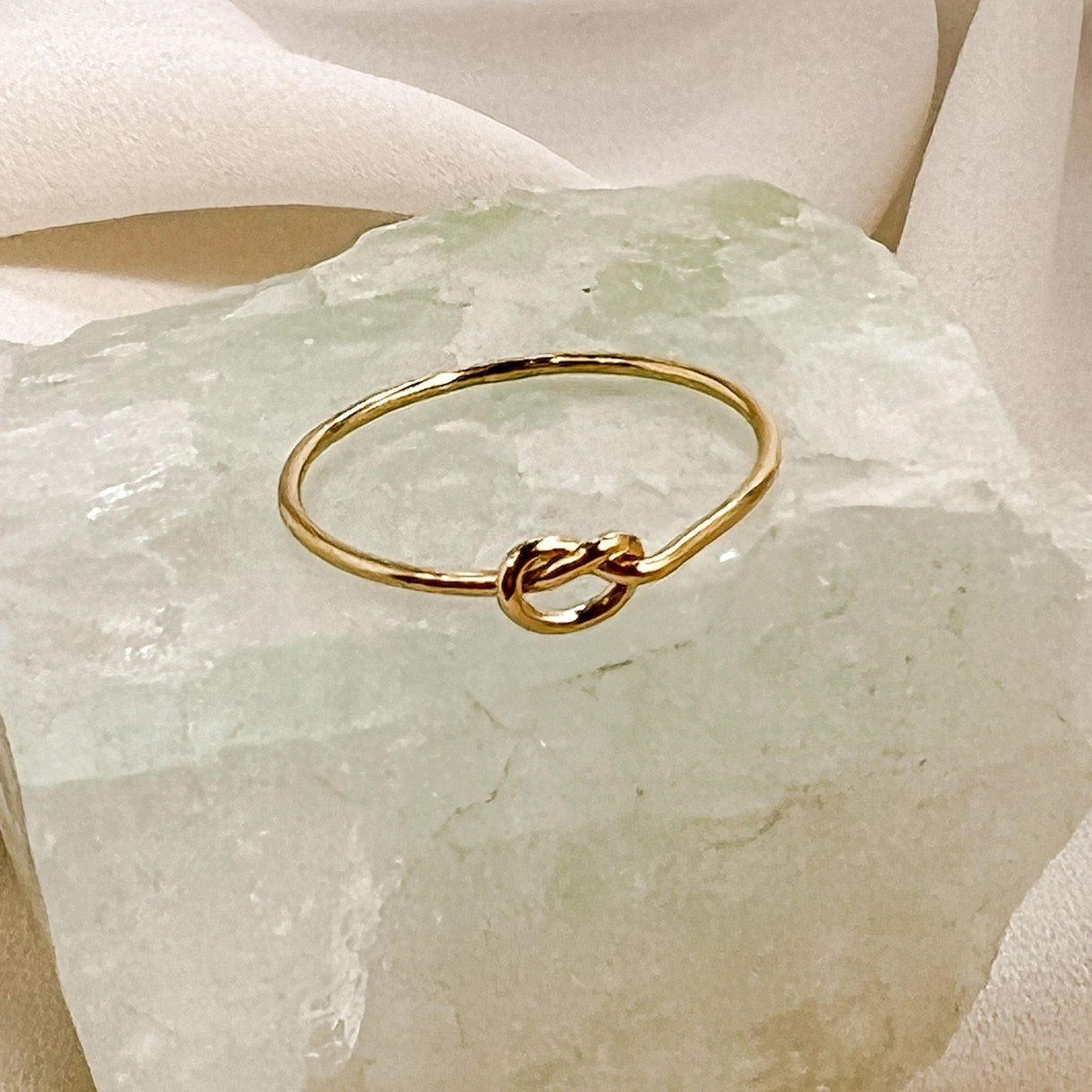 14K gold filled band ring with knot shaped accent. Ring is displayed on an aqua colour gemstone