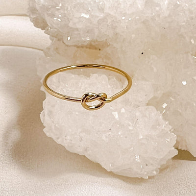 14K gold filled band ring with knot shaped accent. Ring is displayed on a white sparkly crystal geode