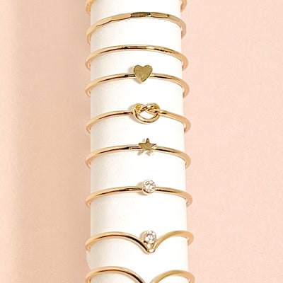 assortment of 8 minimalist stacking rings  displayed on a roll of white paper with a pink background