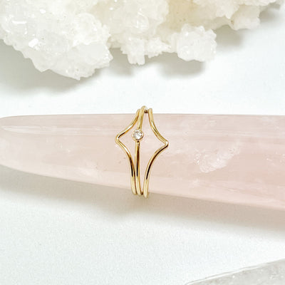 14K gold filled band ring with a 2mm white faceted cubic zirconia accent stone displayed between two chevron styled gold stacking rings to create a triple ring stack displayed on rose quartz gemstone