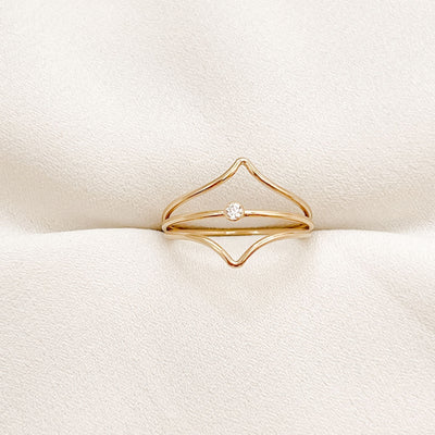 14K gold filled band ring with a 2mm white faceted cubic zirconia accent stone displayed between two chevron styled gold stacking rings to create a triple ring stack displayed on cream coloured fabric