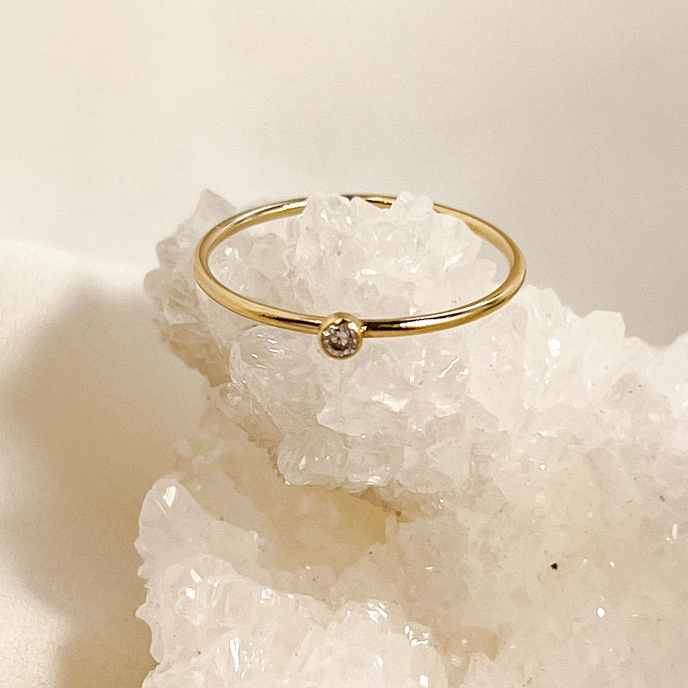 14K gold filled band ring with a 2mm white faceted cubic zirconia accent stone displayed on white sparkly crystal geode