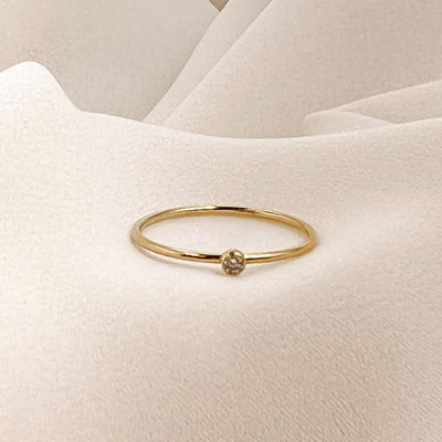 14K gold filled band ring with a 2mm white faceted cubic zirconia accent stone displayed on cream coloured fabric