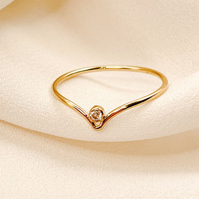 14K gold filled chevron shaped ring with white sparkly cubic Zirconia stone nestled into the center point of the chevron peak. on cream colored fabric 