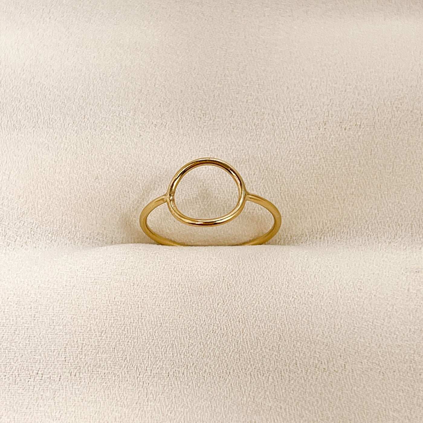 highly polished, dainty 14KGF hollow circle stacking ring displayed on cream coloured fabric