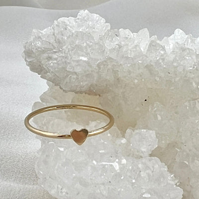 14K Gold filled simple band ring with tiny 2mm cut out heart shape on top. Gold heart ring is sitting onto of shiny white crystal