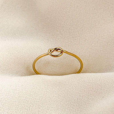 14K gold filled band ring with knot shaped accent. Ring is on cream coloured fabric