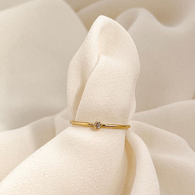 14K gold filled band ring with a 2mm white faceted cubic zirconia accent stone displayed on cream coloured fabric