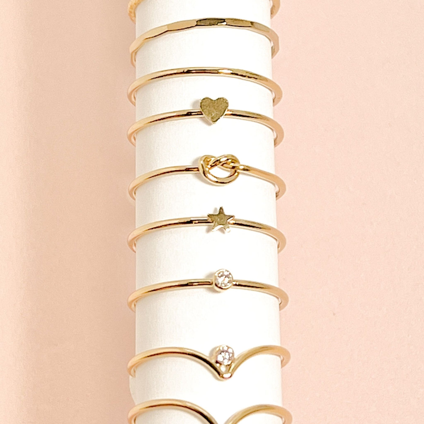 Assortment of differing styles of minimalist and dainty women’s stacking rings displayed on white roll of paper 