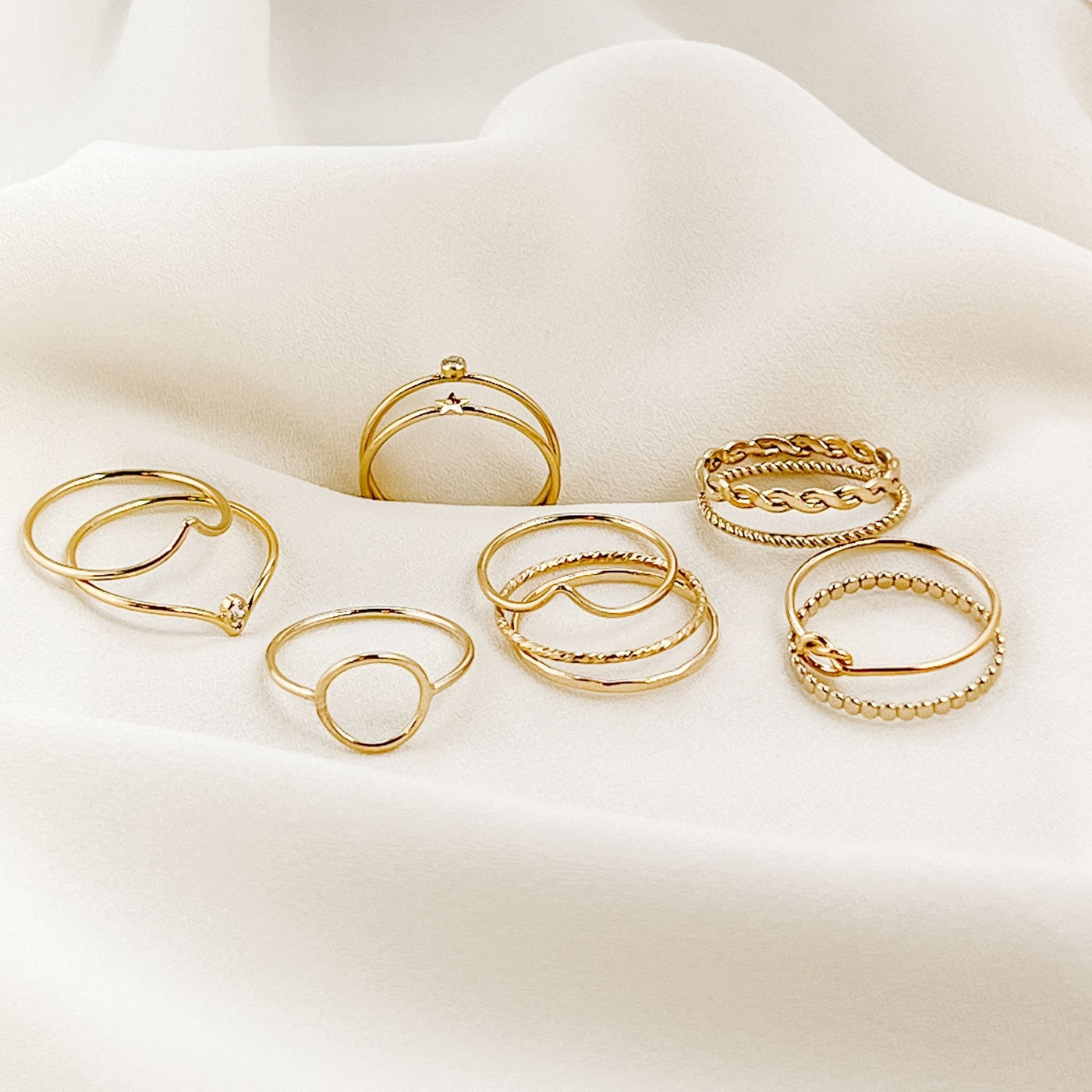 Assortment of 12 minimalist 14KGF stacking rings displayed on cream colored fabric 