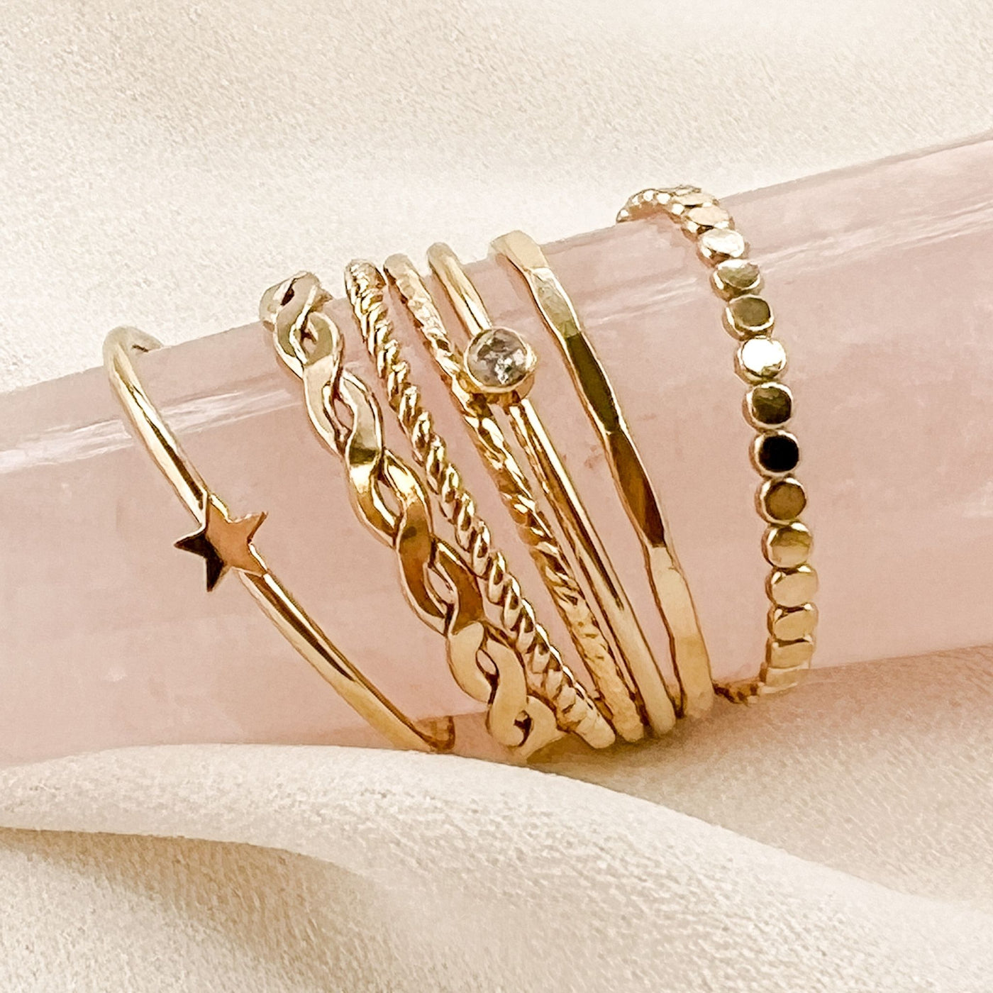 Assortment of differing styles of minimalist and dainty women’s stacking rings displayed on pink rose quartz crystal