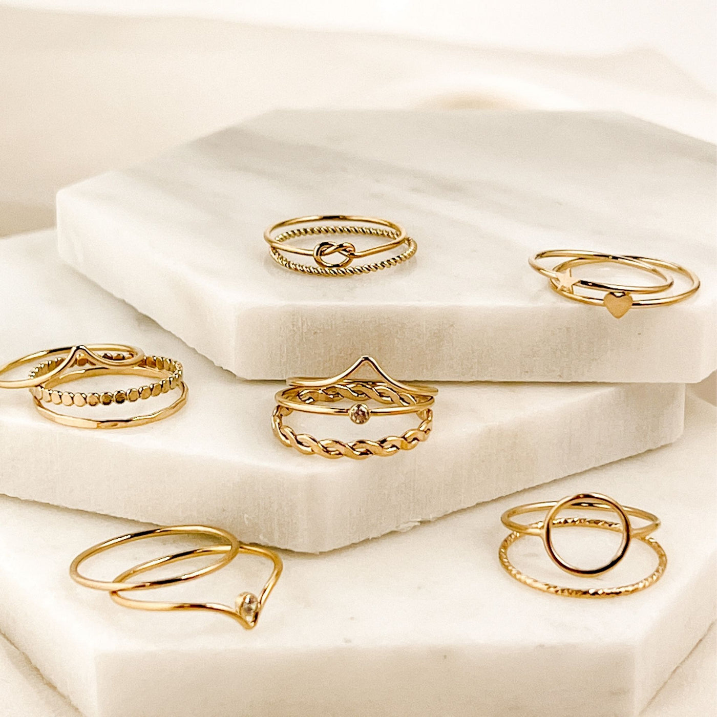 Assortment of 14 minimalist 14KGF stacking rings displayed on three tiered hexagonal shaped marble tiles  