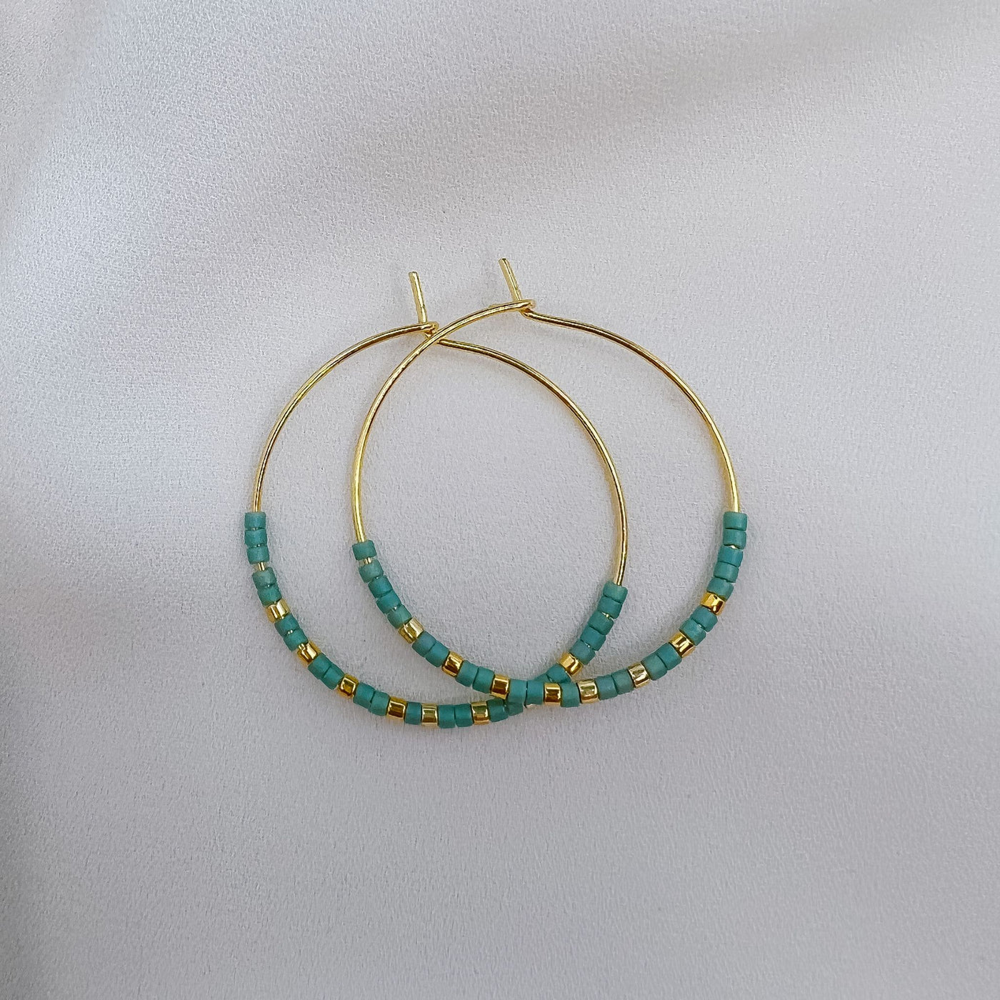 Teal coloured miyuki beads on a gold hoop earring with gold bead accents